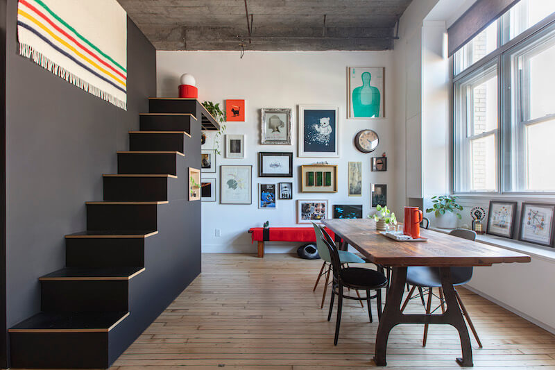 Loft dining area with gallery wall, black mezzanine stair, exposed concrete ceiling