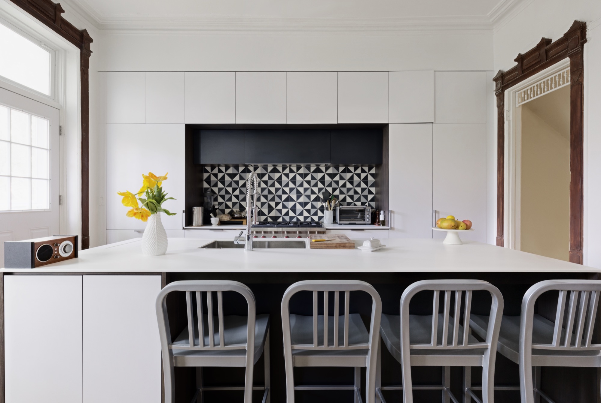 White flat-front kitchen with graphic black-and-white tile inside preserved period casings