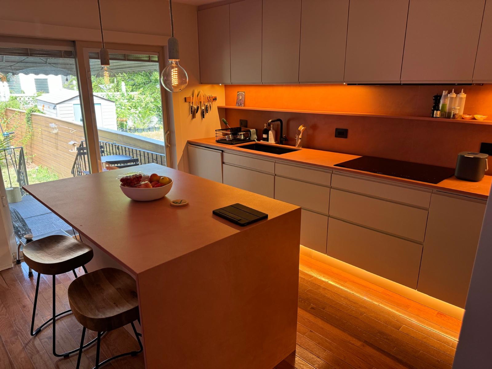 Modern handleless kitchen with terracotta waterfall island and garden doors open to the backyard