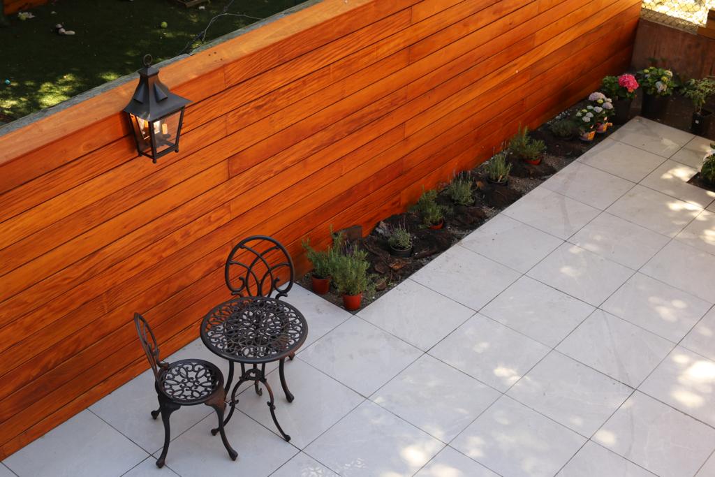 Rear garden with horizontal hardwood fence running past stone paving and planted borders