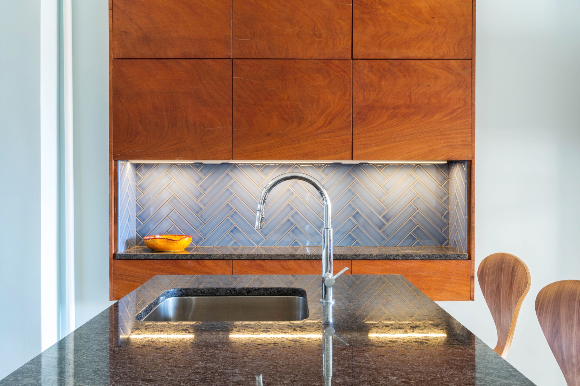 Mahogany upper cabinets and blue herringbone glass tile over a black stone counter